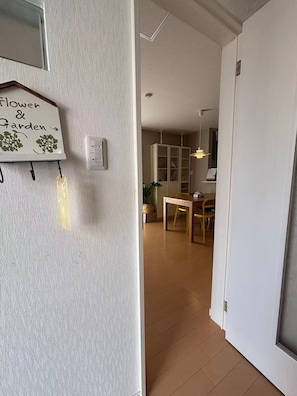 A hallway with a white wall, a sign reading 'Flower & Garden', and a wooden table with chairs in the background.