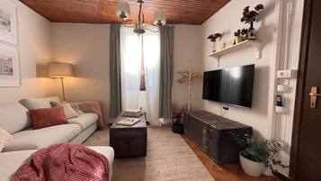 A living room with a sofa, a coffee table, a TV, and a wooden ceiling.