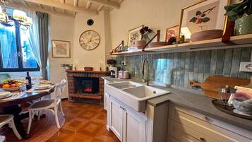 A kitchen with a sink, wooden cabinets, a dining table with chairs, a clock, and a fireplace.