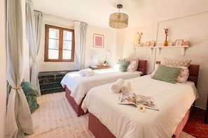 A hotel room with two beds, a window with curtains, a bedside table with a lamp, and a shelf with decorative items. - La Fetta Di Cima (Porlezza)