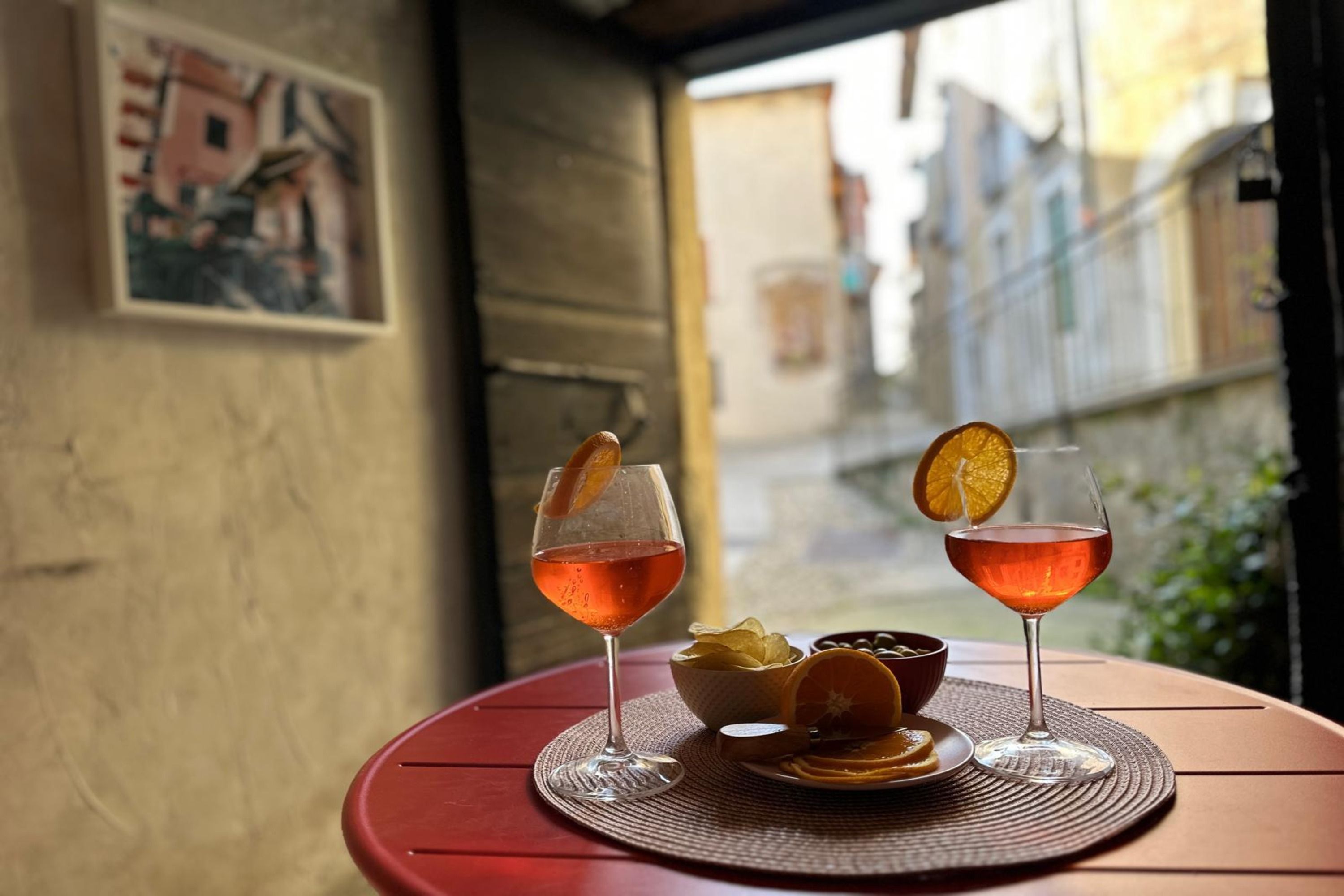 Two glasses of a red beverage on a table with a bowl of chips and a plate of orange slices.