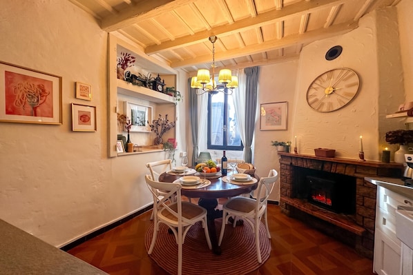 A dining area with a round table, white chairs, a chandelier, a fireplace, and framed artwork on the walls. - La Fetta Di Cima (Porlezza)