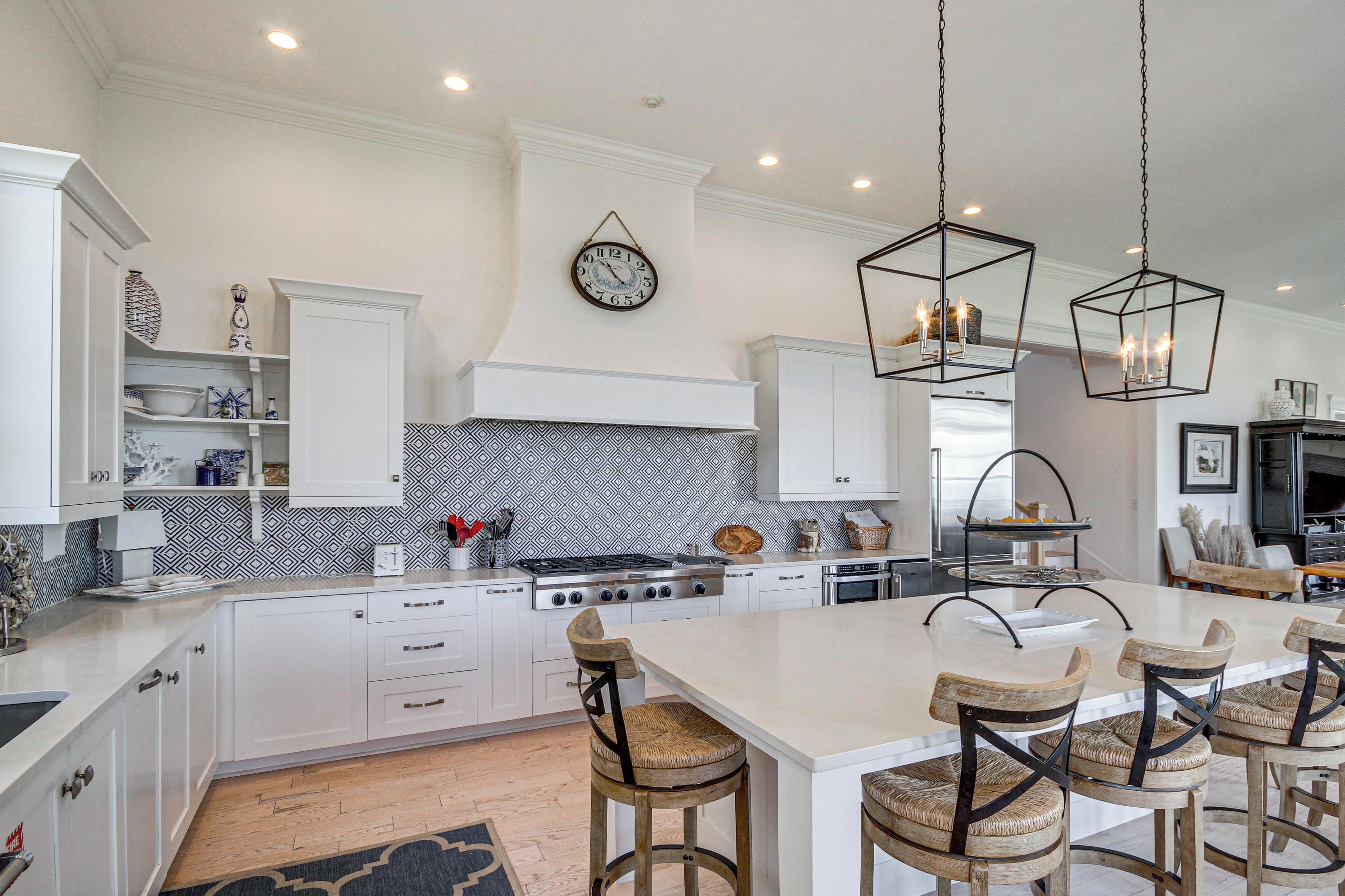 Une cuisine moderne avec des meubles blancs, un îlot central doté de tabourets, un pare-feu décoratif et des luminaires suspendus.