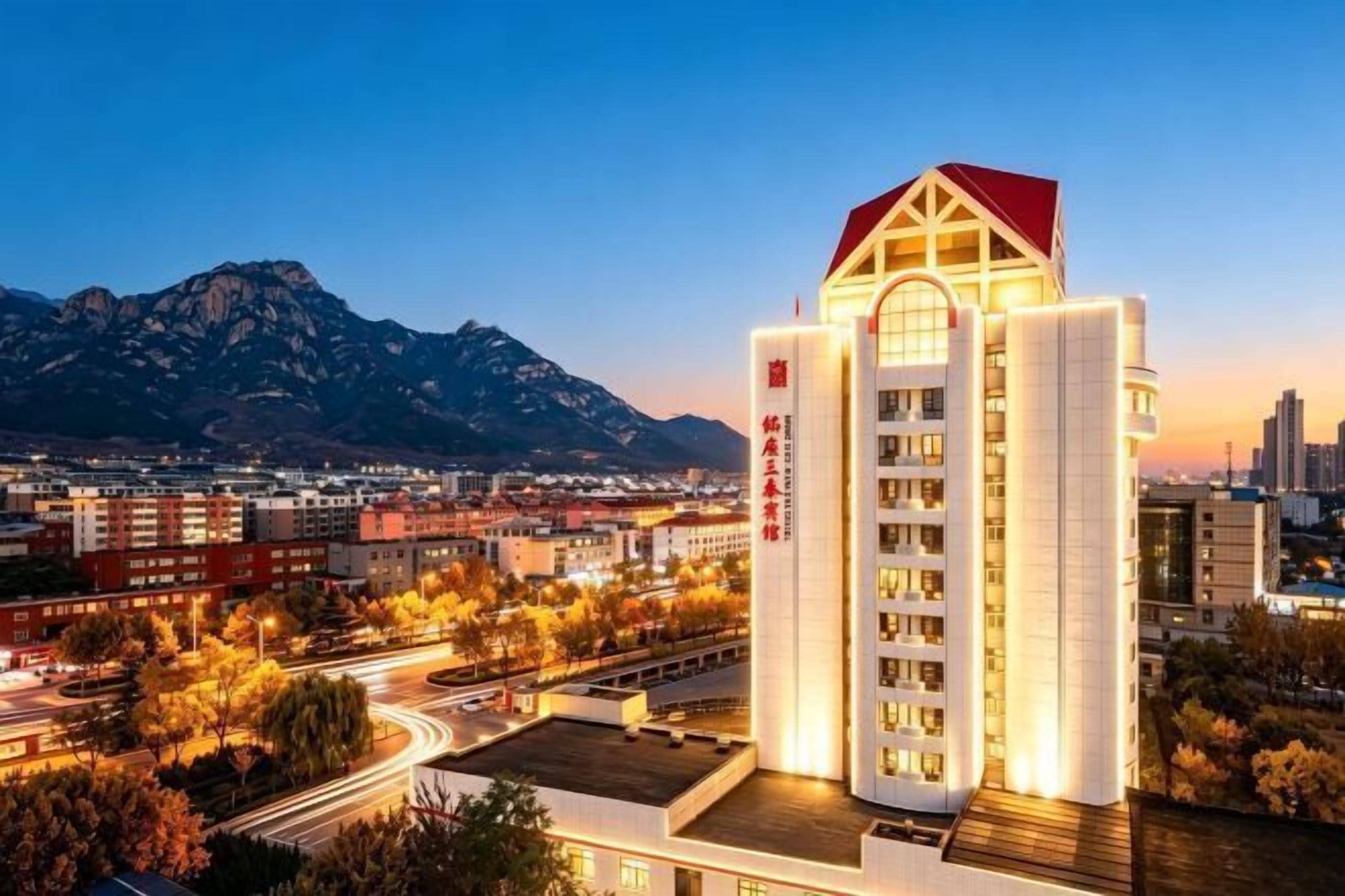 A hotel with a prominent red roof, multiple floors, and a view of a mountainous landscape in the background.
