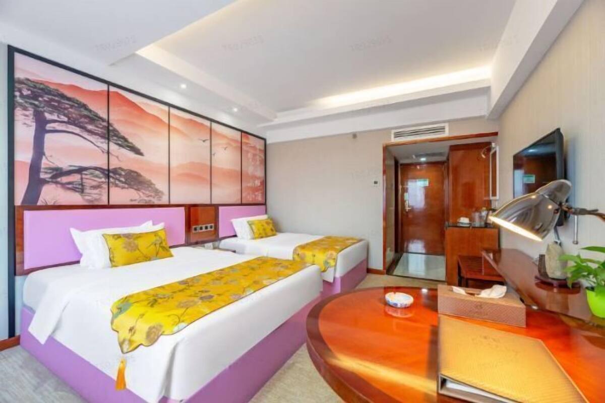 Quarto de hotel com duas camas, uma escrivaninha, um espelho e um quadro grande na parede.