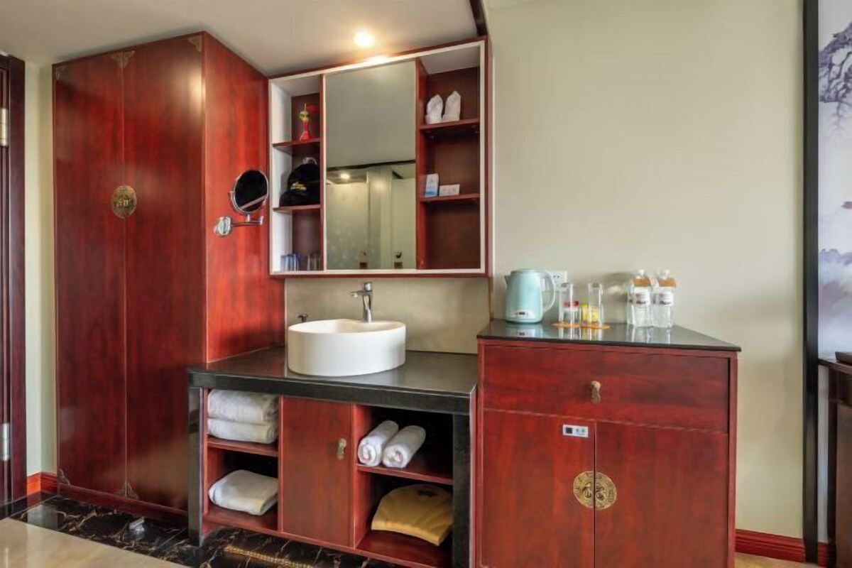 A bathroom with a wooden vanity, a sink, a mirror, and shelves with towels.