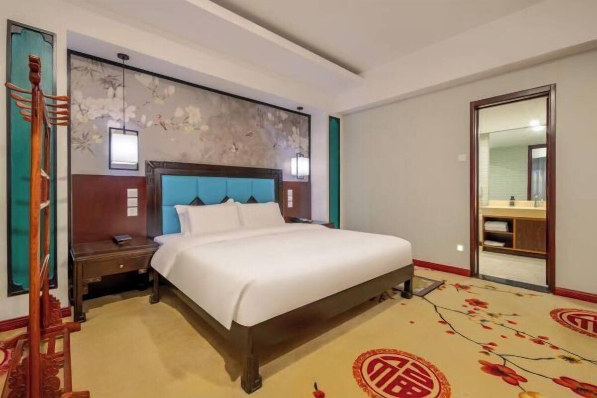 Quarto de hotel com uma cama, mesa de cabeceira, espelho e escada de madeira.