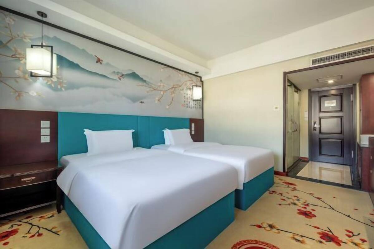 Quarto de hotel com duas camas, um mural na parede e uma porta que dá para outro cômodo.