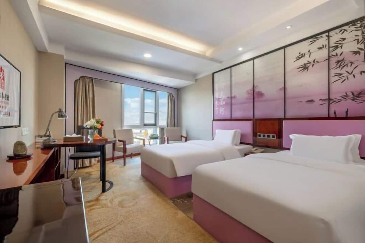 Habitación de hotel con dos camas, un escritorio, una silla, una ventana y un panel decorativo en la pared.