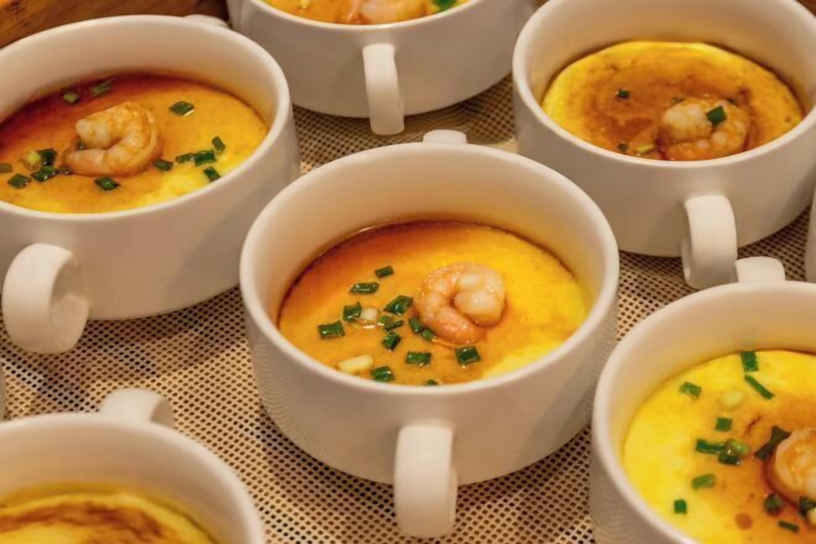Vários copos de cerâmica branca com sopa cremosa e enfeite de camarão.