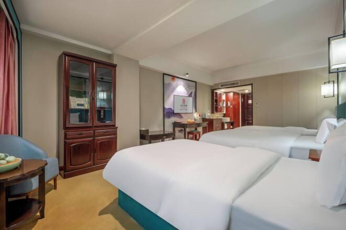Quarto de hotel com duas camas, um armário de madeira, uma escrivaninha e um espelho.