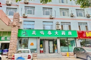 A building with multiple air conditioning units, a green sign with white text, and a parked car in front. - Tai'an Mingzuo Santai Theme Hotel (Taishan Scenic Area) (Tai'an)