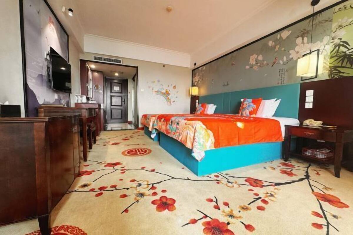 Quarto de hotel com uma cama, uma escrivaninha, uma televisão e uma parede com obras de arte florais.
