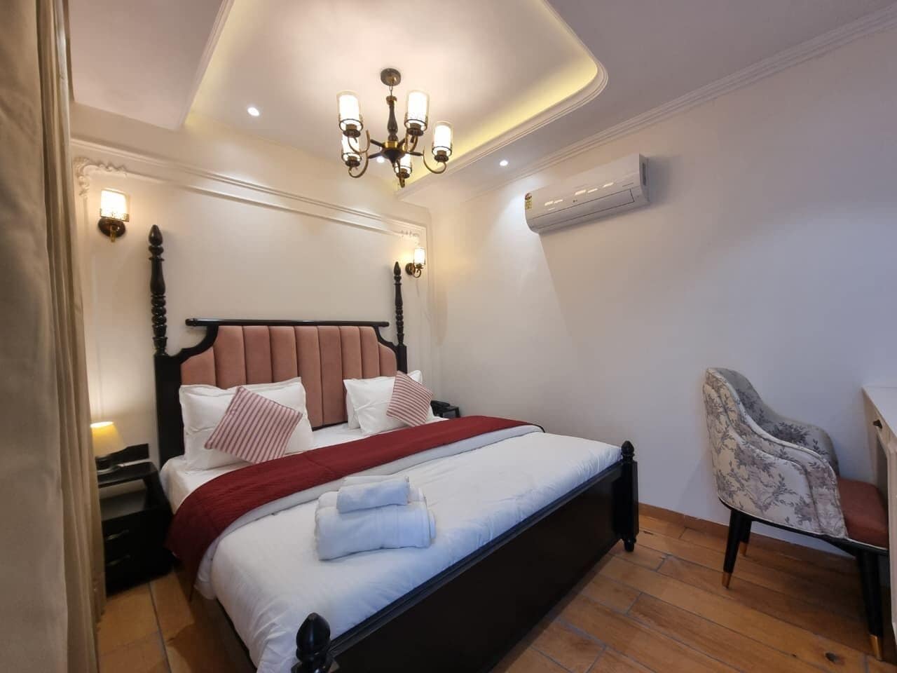 Una cama bien hecha con cabecera, lámpara de noche y una silla.