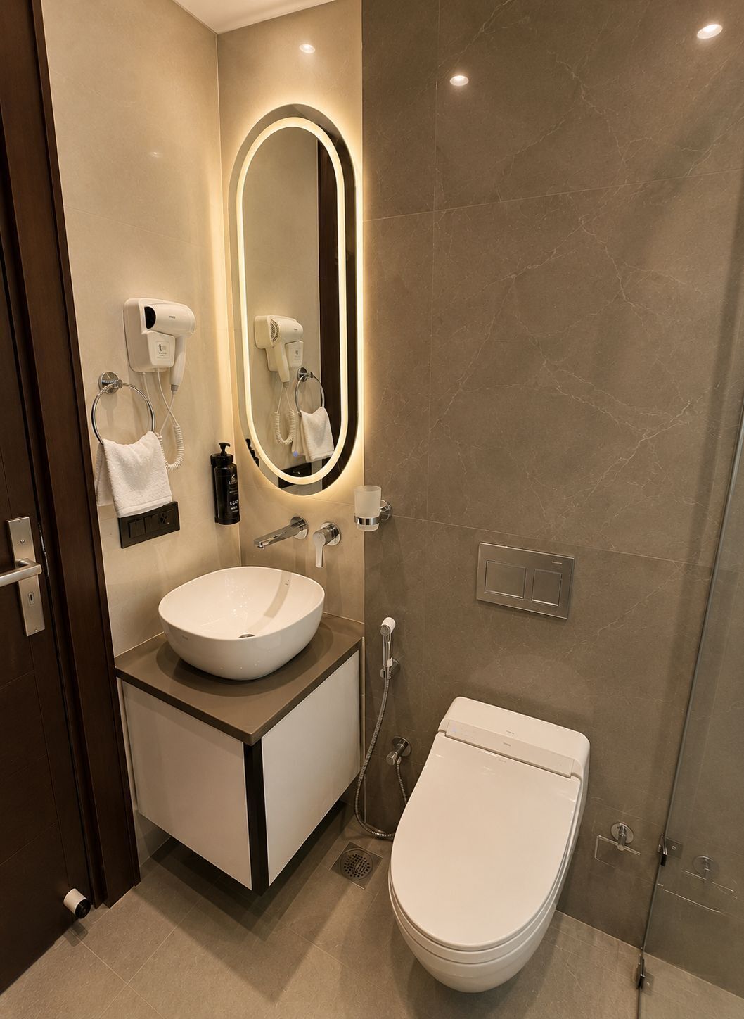 A modern bathroom with a round sink, a toilet, and a mirror with built-in lighting.