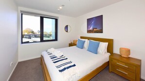 Un dormitorio con una cama grande, una mesita de noche, un ventanal y un cuadro colgado en la pared.