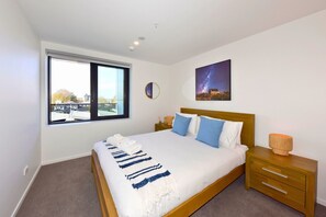A bedroom with a large bed, a bedside table, a nightstand, a window, and a wall-mounted picture. - Chic and Stylish 1BR Apartment in Manchester Street (Christchurch)
