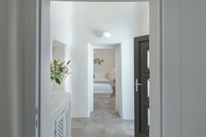 A hallway leading to a bedroom with a bed, a wall-mounted light fixture, and a decorative wall piece. - 3 Bedroom Villa with Outdoor Hot Tub & Sea View, Aleanna Traditional Villa (Santorini)