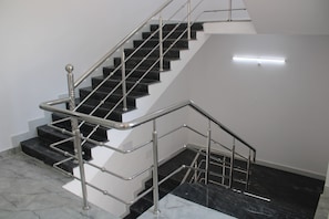 Eine Treppe mit Metallgeländer und schwarzen Stufen, die zu einer Zwischenebene mit einer Leuchte führt.