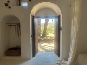 A room with an arched doorway leading to an outdoor area, a wooden bench, and a hanging coat rack. - ANCIENT RURAL DAMMUSO WITH POOL AND SEA VIEW (Pantelleria)
