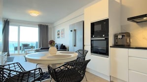 Een moderne keuken met een ingebouwde oven, een koffieapparaat en een eethoek met een ronde tafel en stoelen.