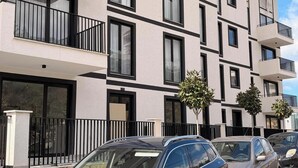 Een meerlaags woongebouw met balkons, grote ramen en een parkeerplaats met auto's.