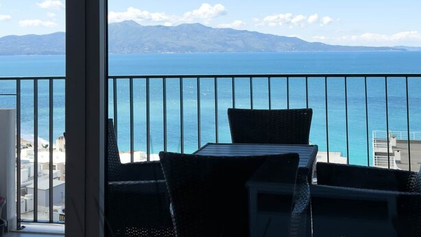 Een balkon met uitzicht op zee en bergen, een tafel en stoelen.
