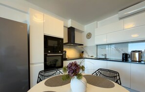 A modern kitchen with white cabinetry, a black range hood, a microwave, and a clock on the wall. - Elisa - Panoramic View (Saranda)