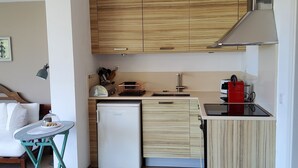 Een moderne keuken met houten kastjes, een kleine koelkast, een spoelbak, een koffieapparaat en een prullenbak.