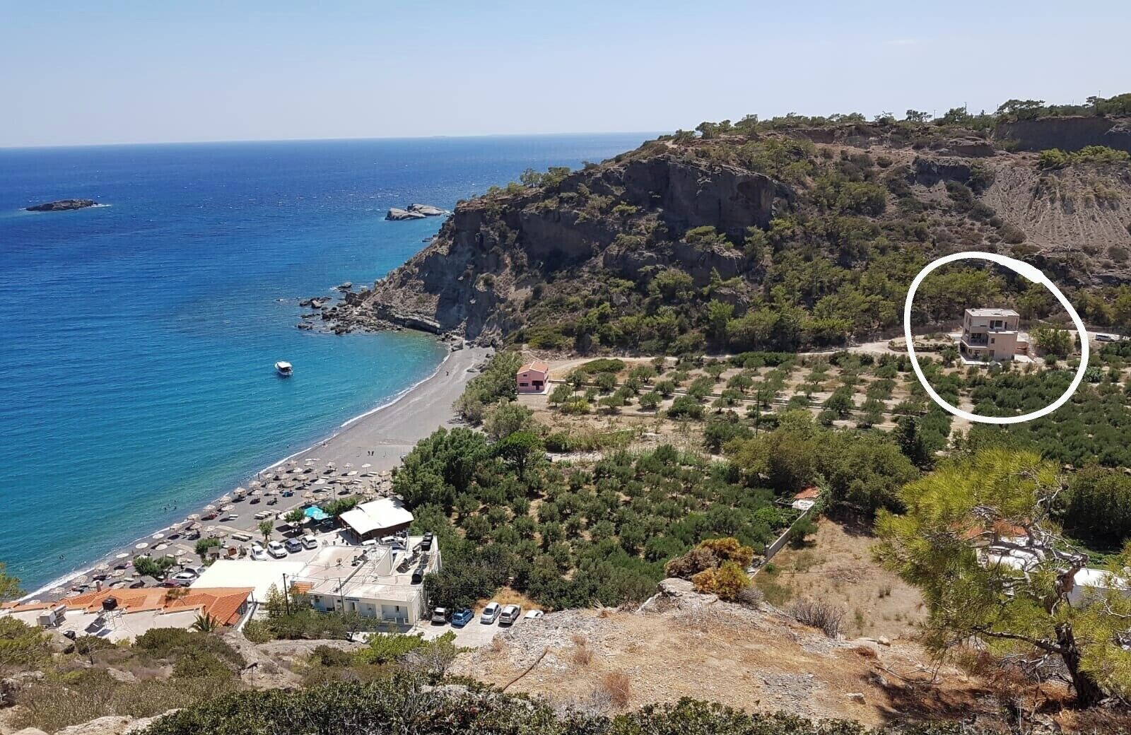 Un paisaje costero con una playa, acantilados rocosos y un edificio señalado en la esquina superior derecha.
