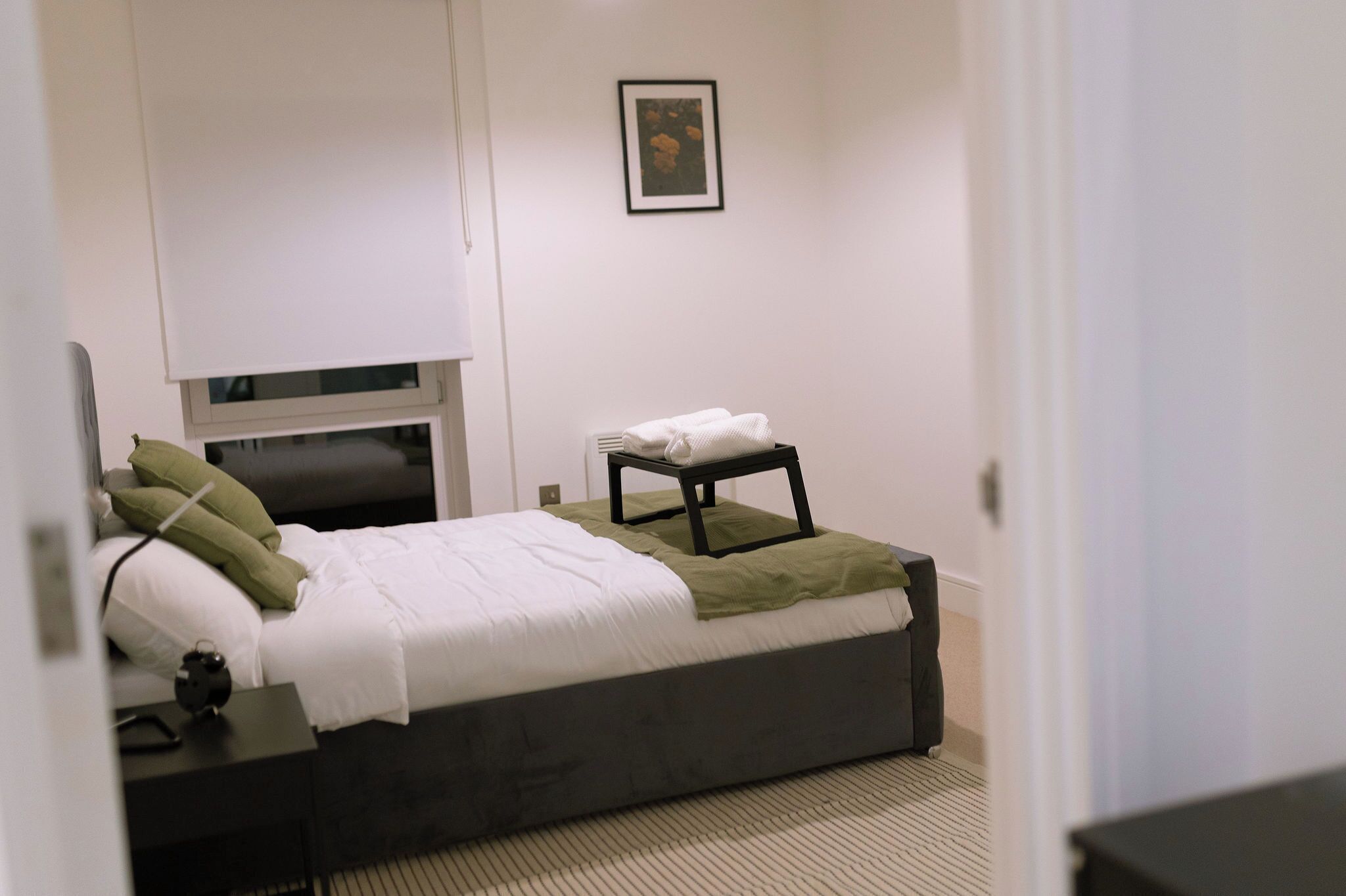 A bedroom with a bed, bedside table, and a small stool.