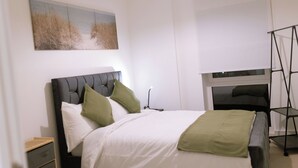 Ein Schlafzimmer mit Bett, Nachttischen, einer Hängeleuchte, einem Gemälde und einem Fernsehschrank.