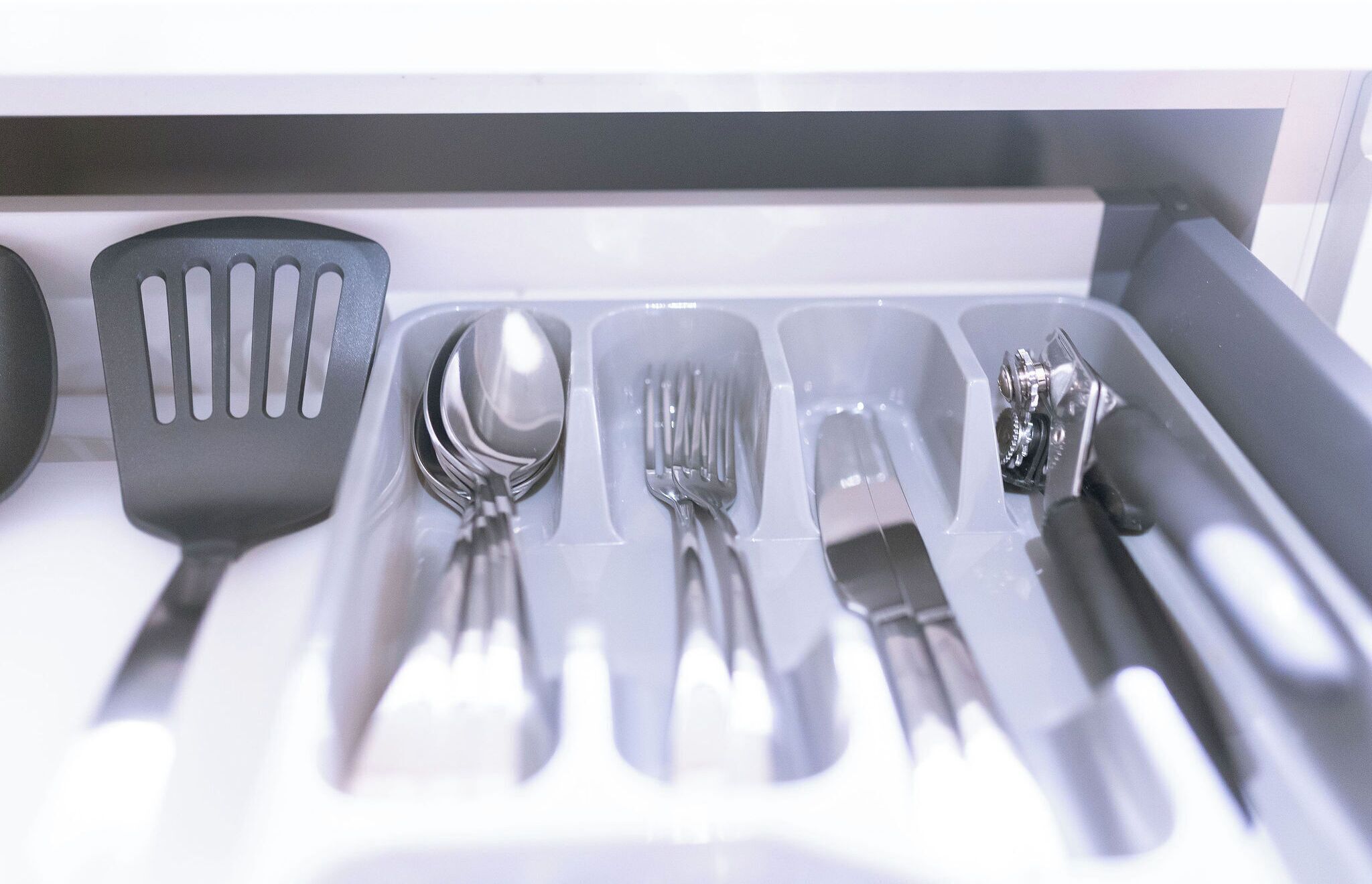 A kitchen drawer with utensils including a spatula, spoon, fork, knife, and grater.