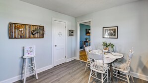Een eetgedeelte met een ronde tafel, witte stoelen en een klein wit tafeltje met een lijstfoto.