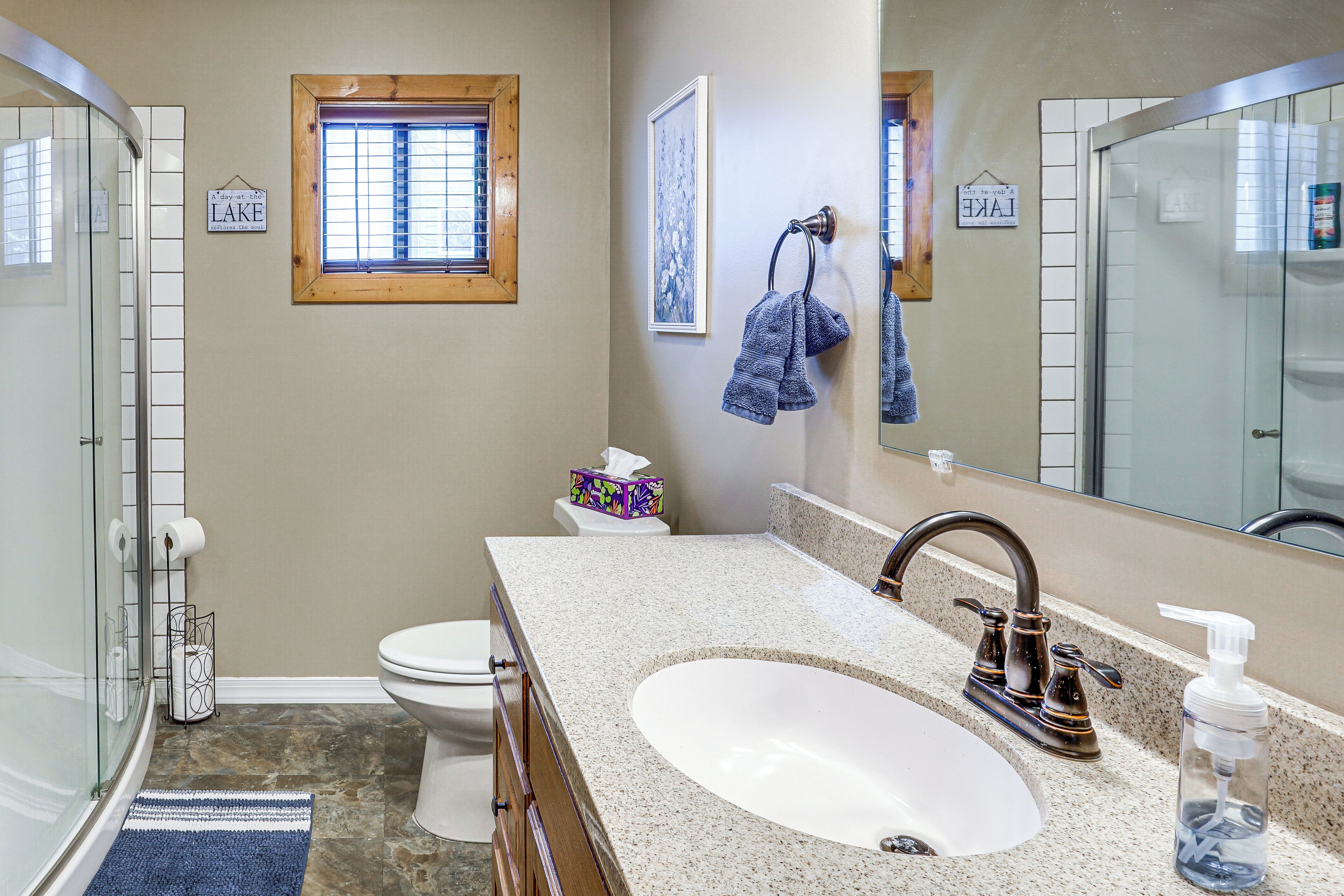 A bathroom with a glass shower enclosure, a sink with a faucet, a toilet, and a window with blinds.