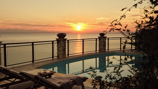 A poolside area with lounge chairs, a stone balustrade, and a view of the sunset over the sea. - Villa Yiannis - Sea View & Private Pool (Zakynthos)