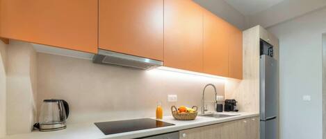 A modern kitchen with orange cabinets, a stainless steel refrigerator, a coffee maker, and a fruit basket.