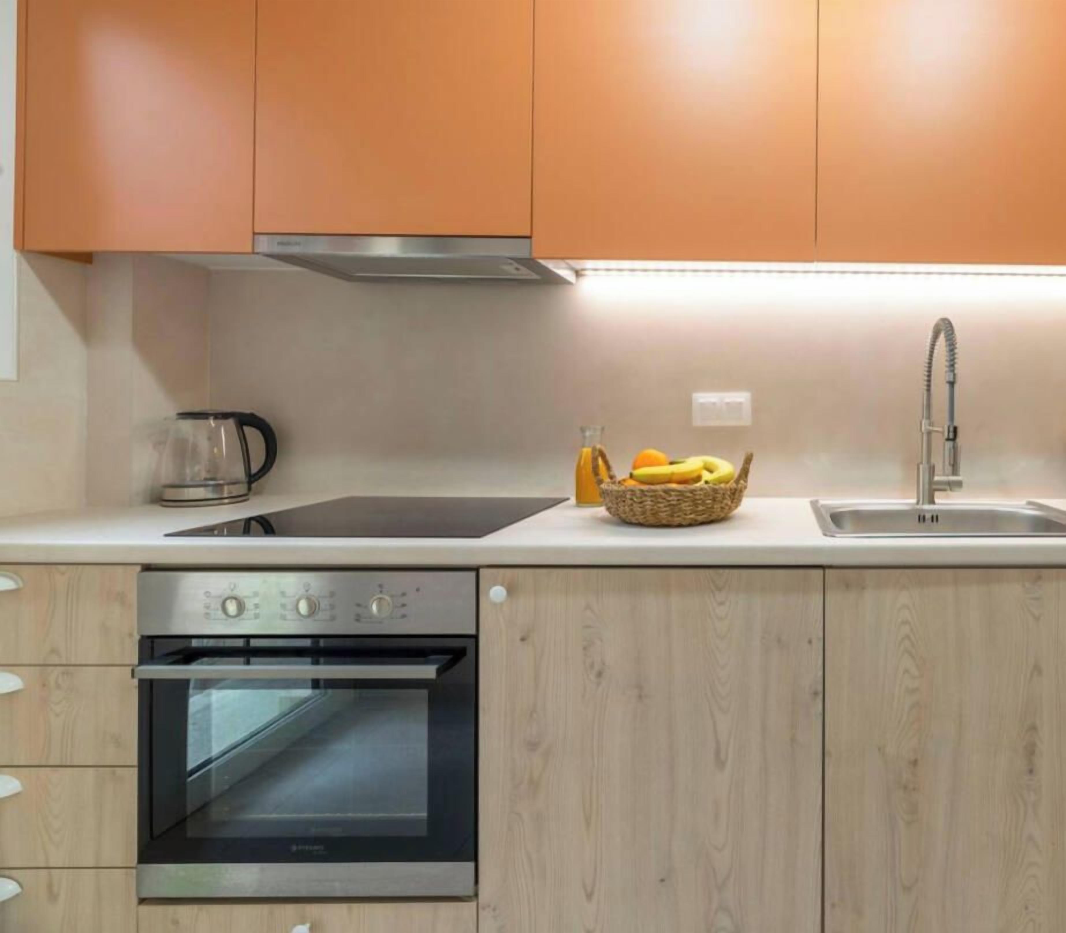 A kitchen with wooden cabinets, a stainless steel oven, a sink, and a basket of fruit on the countertop.