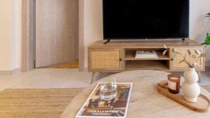 Uma sala de estar moderna com televisão de tela plana, um aparador de madeira, uma revista sobre uma mesa de centro e uma vela.