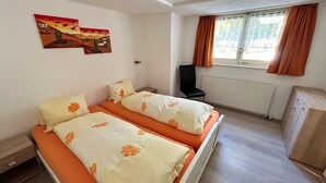 Habitación con dos camas, una silla, un radiador y una ventana con cortinas.