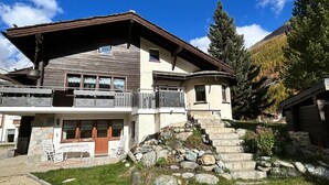 Un chalet de dos plantas con fachada de piedra, balcón de madera y una escalera de piedra que conduce a la entrada.