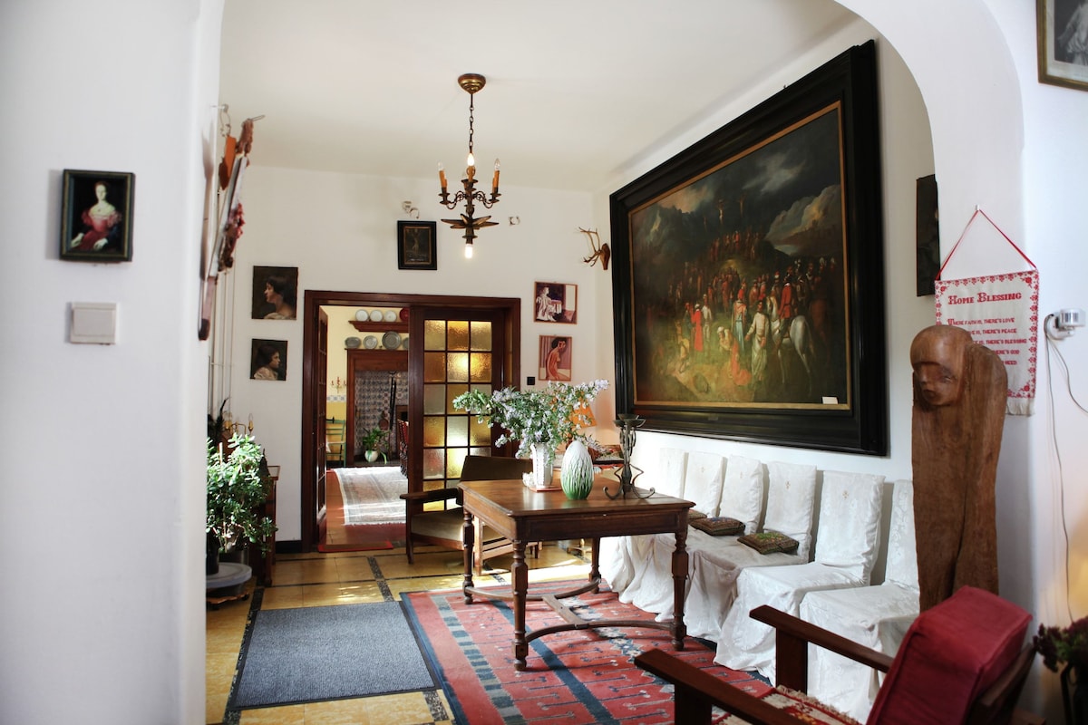 A traditional living room with a chandelier, a large painting, and a wooden table.