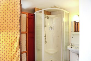 Een badkamer met een douchecabine van glas, een witte wastafel en een houten kastje.