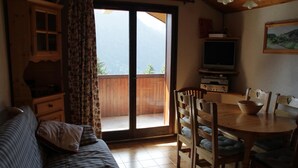 A cozy room with a sofa, a dining table with chairs, a television, and a sliding glass door leading to a balcony. - Apartment in Chatel Near Cable Car (Chatel)