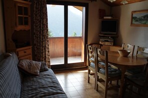 A cozy room with a sofa, a dining table with chairs, a television, and a sliding glass door leading to a balcony. - Apartment in Chatel Near Cable Car (Chatel)