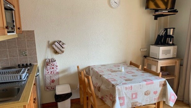 A kitchen with a stove, microwave, and coffee maker, a table with chairs, a clock, and a television on a shelf. - Apartment in Chatel Near Cable Car (Chatel)