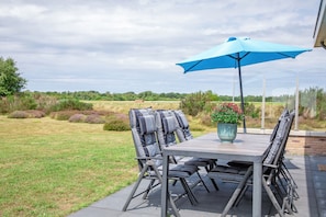 An outdoor patio with a table, chairs, and a blue umbrella. - Stylish Texel Escape With Spa (Den Burg)