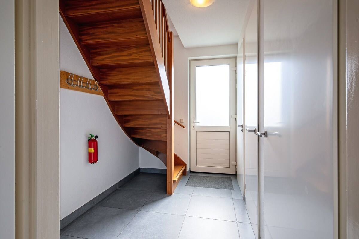 Ein Flur mit einer Holztreppe, einem Feuerlöscher, einer Tür und einem Fenster.