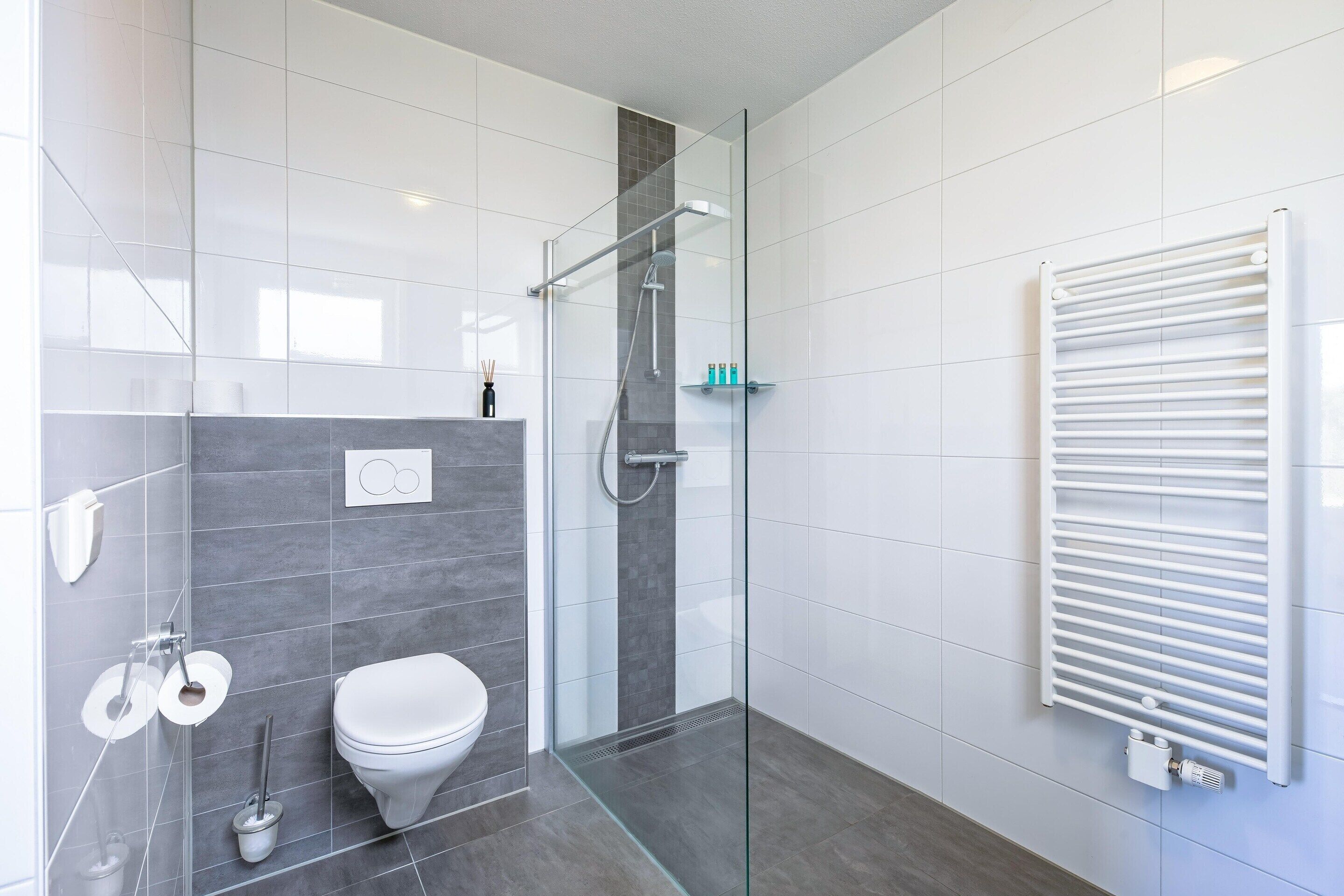 Un baño moderno con cabina de ducha de vidrio, inodoro y toallero empotrado.