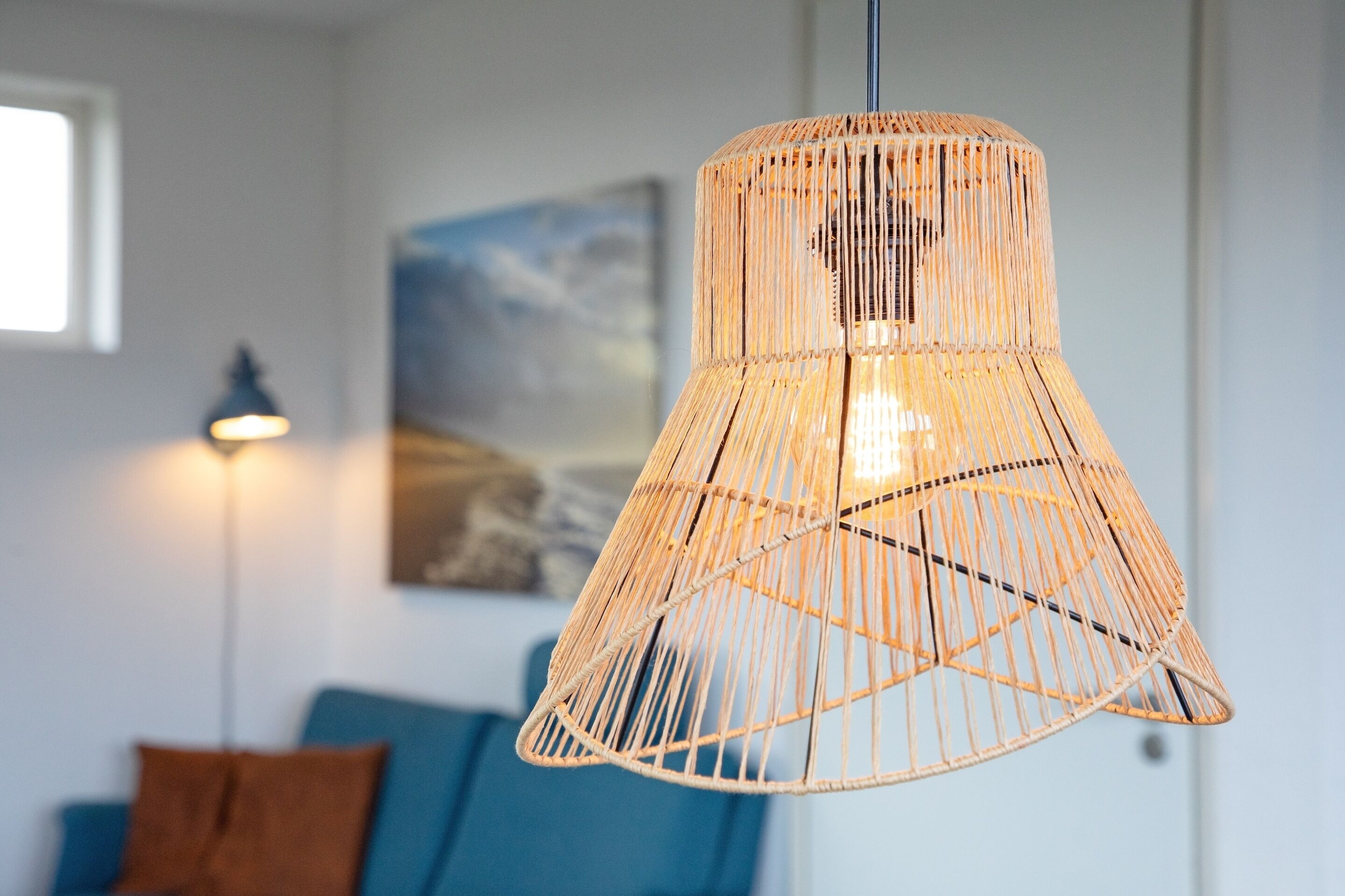 A hanging wicker lamp in a room with a blue sofa and a painting on the wall.